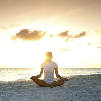 Woman meditating on beach at sunset