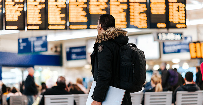 man reading flight screen at airport; cancel for any reason travel insurance covid image