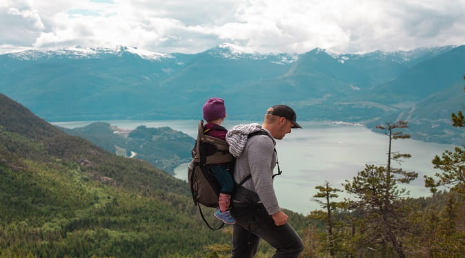 child on back of parent hiking through mountains