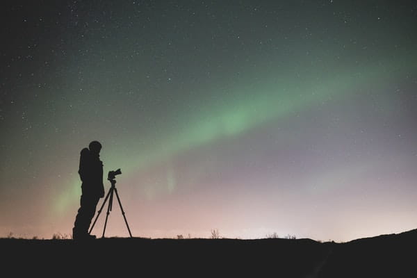 photographer standing with camera under northern lights