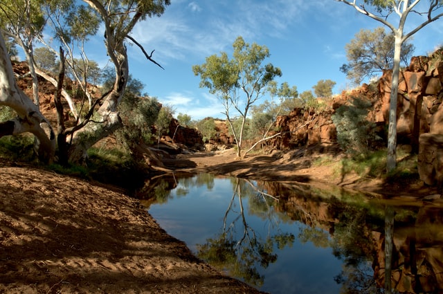pond in the middle of red rocks and trees in the australian outback