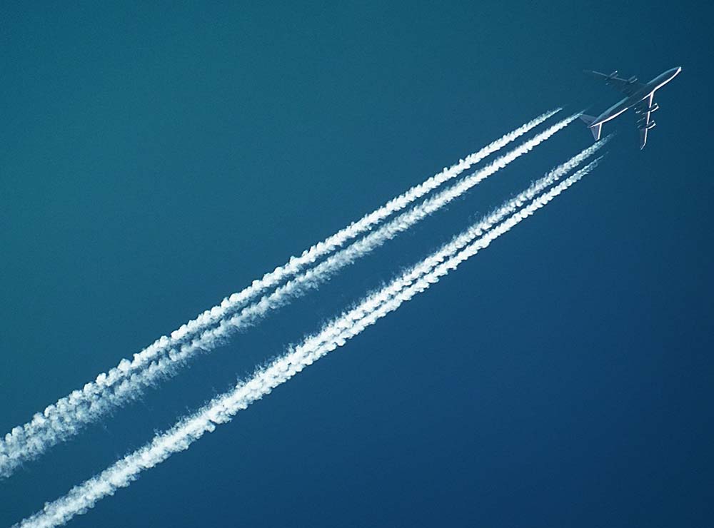 airplane-flying-through-blue-sky-with-trail-carbon-offset-flights