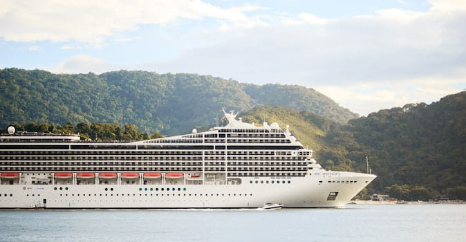 best cruise travel insurance featured image of cruise ship in front of green hills