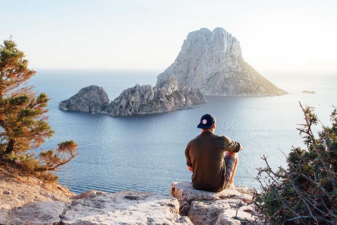person-sitting-on-cliff-looking-at-water-who-should-buy-travel-medical-insurance